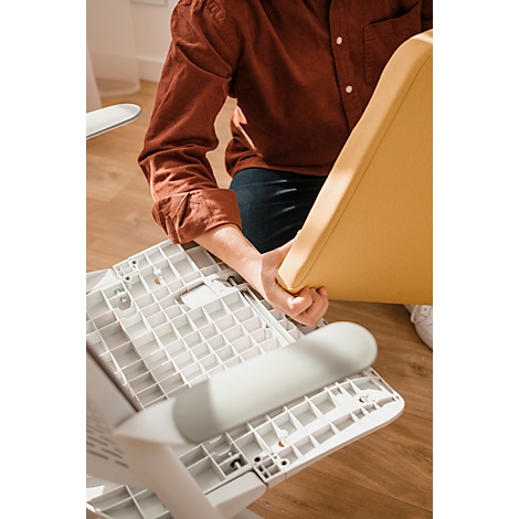 Person assembling chair: Holds yellow seat, which is attached to a white frame. Detailed shot.
