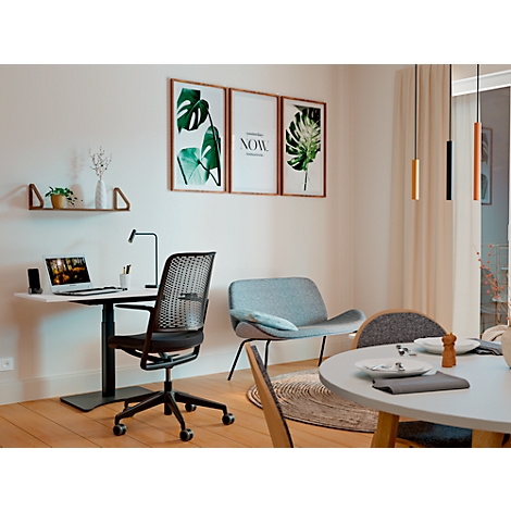 A modern dining room with a desk, a chair, and a sofa. Pictures hang on the wall. There is also a pendant light.