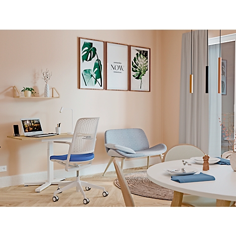 A living room with desk, chair, sofa, and dining table. Pictures hang on the wall, above a shelf with plants. Curtains at the windows.