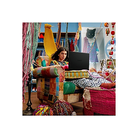 Eine Frau arbeitet an einem Laptop (Omen). Der Raum ist bunt mit Dekorationen. Im Hintergrund eine Katze in einem Kostüm.