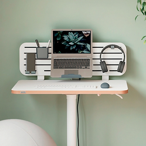 Bureau debout avec ordinateur portable, casque et fournitures de bureau contre un mur vert clair.