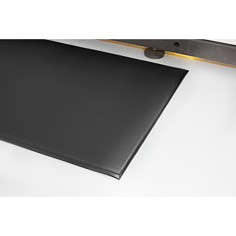 Black, rectangular mat with rounded corners. Shown with part of a structure in the background.
