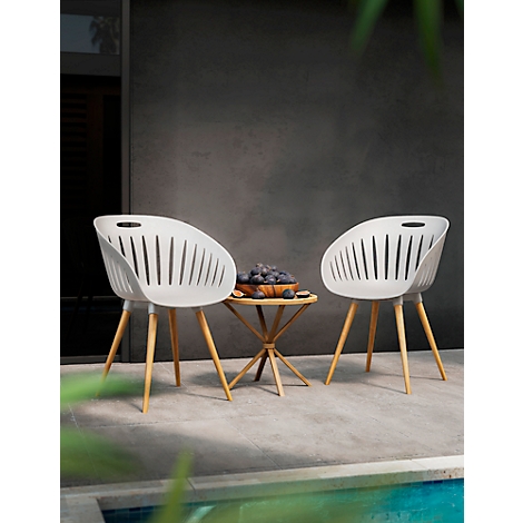 Two white chairs with wooden legs and a table, decorated with fruit, in front of a grey wall.