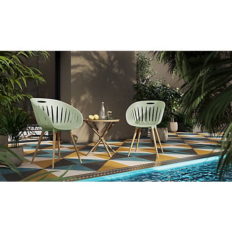 Two green garden chairs with wooden legs stand next to a small table. On the table are fruits and a bottle of water.