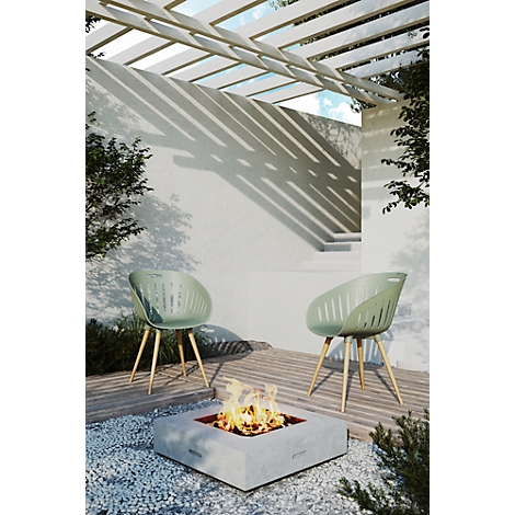 Two green chairs in front of a fire pit. Light casts shadows from a wooden structure above.