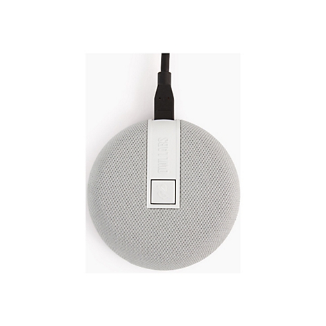 Haut-parleur gris et rond avec surface textile, relié à un câble noir. Sur une surface blanche.