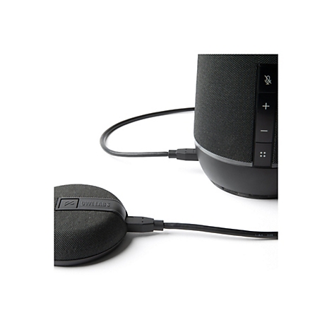 Schwarzer Lautsprecher mit Kabeln, daneben ein runder Lautsprecher mit Schriftzug. Beide sind mit einem USB-Kabel verbunden.