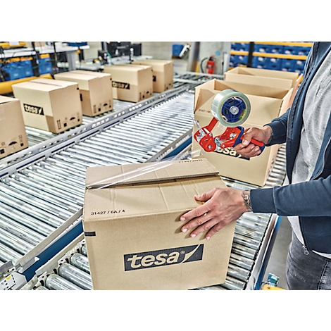 Person verklebt Karton auf Förderband mit tesafilm. Weitere Kartons auf dem Band.