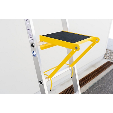 Échelle escabeau jaune avec une surface noire antidérapante. L'échelle est placée devant un mur blanc.