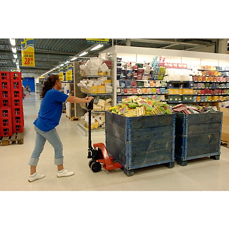 A woman pulls blue wooden crates with a red forklift in a supermarket. The crates are filled with goods.