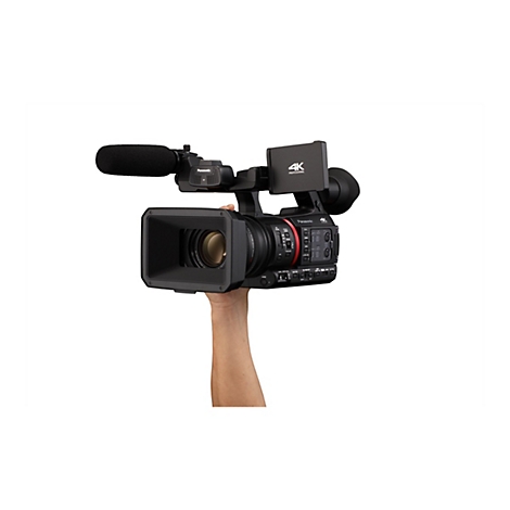 Eine schwarze professionelle Videokamera mit Objektiv, Mikrofon und Haltegriff. Die Kamera wird von einer Hand gehalten, vor weißem Hintergrund.