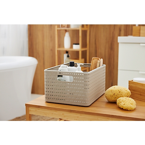 Panier gris avec articles de toilette et brosses sur une surface en bois, articles de salle de bain en arrière-plan.