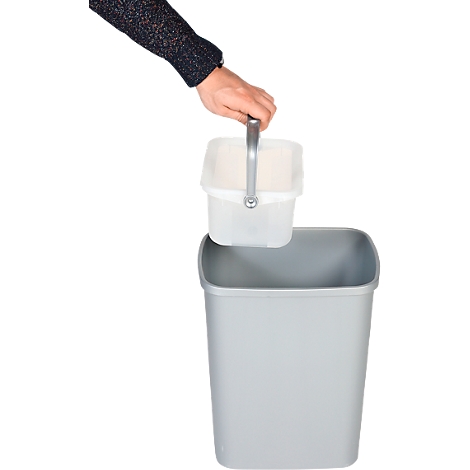 Una mano levanta un pequeño cubo blanco con asa de un cubo de basura gris. El fondo es blanco.