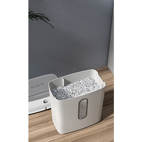 Shredder bin filled with shredded paper. Gray wall on the right, the shredder on the left.