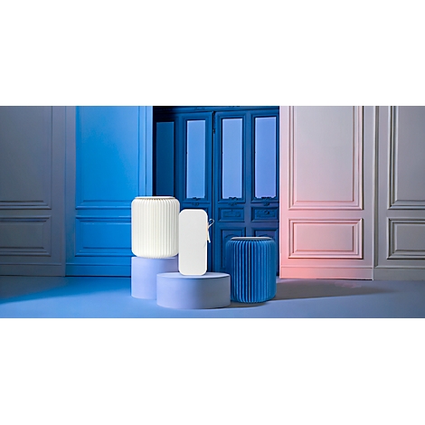 Drie lampen staan op sokkels tegen een achtergrond van deuren en muren. Twee lampen zijn verlicht, één blauw, één wit.