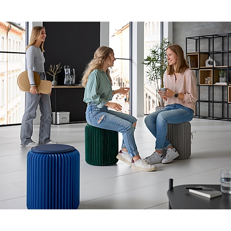 Drie jonge vrouwen zitten en staan in een moderne kamer. Ze praten met elkaar, een van de vrouwen houdt een kruk vast.