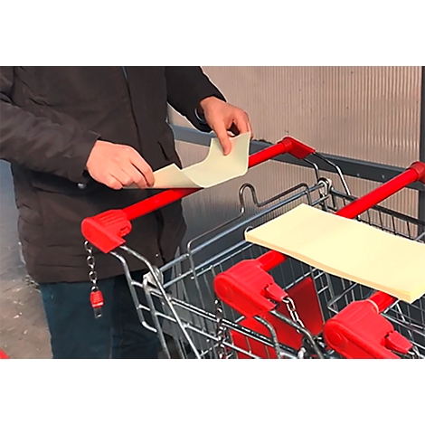 Une personne place du papier sur la poignée d'un chariot de magasinage. Poignée et support rouges.