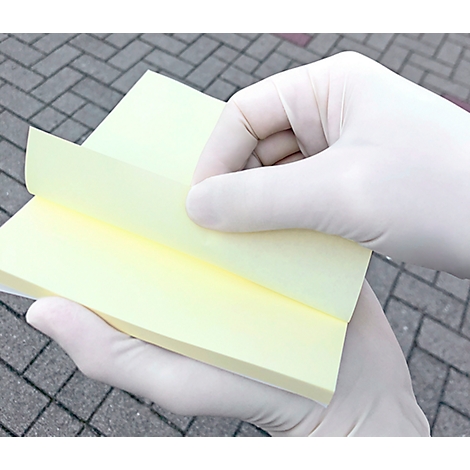 Des mains gantées de blanc soulèvent un feuillet jaune. En arrière-plan, un chemin pavé est visible.