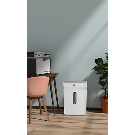 Witte papierversnipperaar in een kantoor met stoel, printer en plant. De kamer is blauw en heeft een houten vloer.