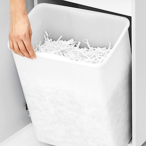 Een hand houdt de witte papierbak van een shredder machine vast. De bak is gevuld met versnipperd papier.