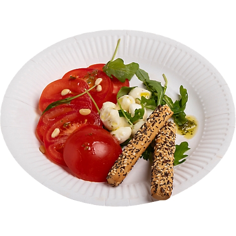 Ein Teller mit Tomatensalat, Mozzarella, Rucola und Brotstangen. Die Tomaten sind in Scheiben geschnitten.