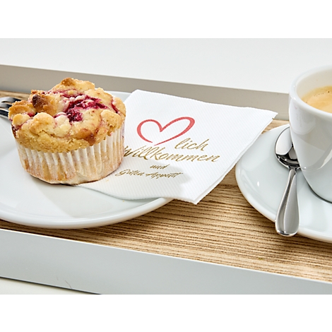 Ein Muffin mit Himbeeren liegt auf einem Teller neben einem Kaffee. Ein Servietten mit Herz und Willkommensgruss liegt auf dem Tablett.