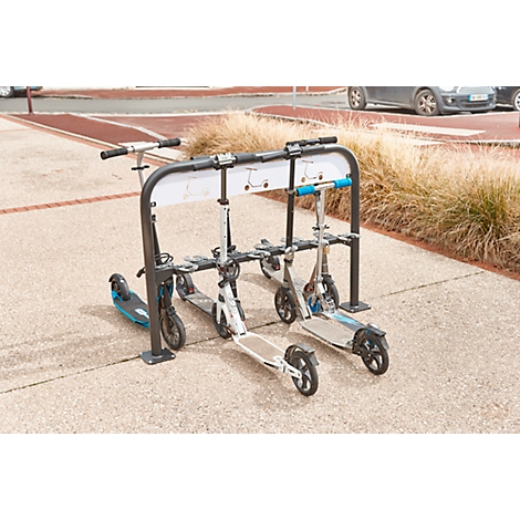 Scooters parked in a stand. Behind them is a sidewalk, to the right dry grass and in the background cars.