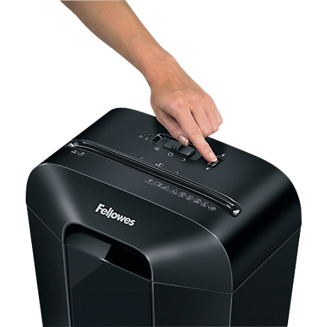 A hand presses the start button of a black Fellowes shredder.