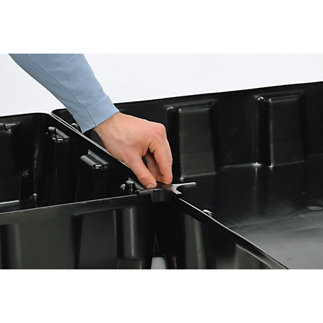 Eine Hand legt eine Metallplatte in eine schwarze Box ein. Die Platte hat einen gebogenen Haken.