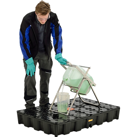 Man pours liquid from a container into a beaker on a black containment tray. He wears safety glasses and gloves.