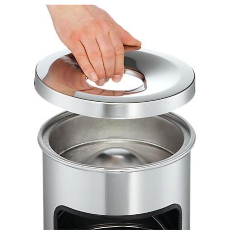 A hand lifts the lid of a stainless steel trash can.