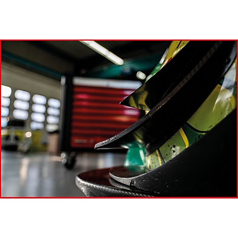 Detailaufnahme eines schwarzen Teils eines Rennwagens. Im Hintergrund verschwommene Garage.