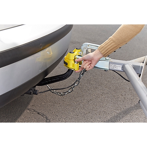 Person connecting trailer hitch with yellow safety lock on the car.