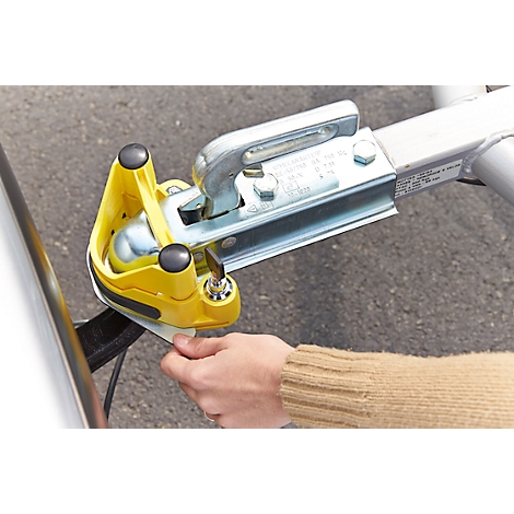 A person is operating a yellow trailer hitch lock on a silver trailer hitch.