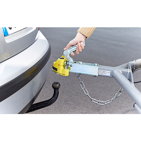 Close-up of a car with a trailer hitch. A hand is connecting the trailer hitch to a trailer.