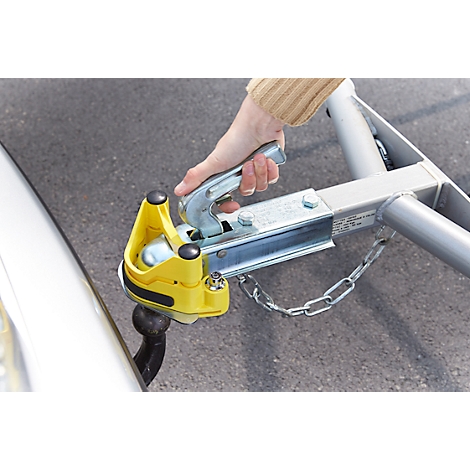 A person connecting a yellow trailer to a silver tow hitch. The hand is holding the latch.