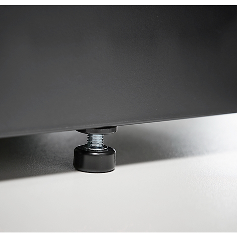 Gros plan d'un pied de meuble réglable. Un pied noir et cylindrique avec filetage et rondelle, sous un meuble gris.