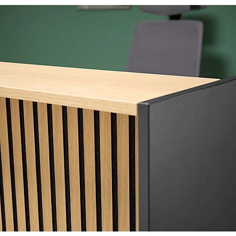Gros plan d'une réception en bois avec des rayures noires verticales et un panneau latéral noir. Une chaise de bureau et un mur vert sont visibles en arrière-plan.