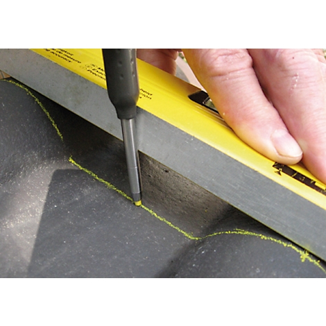 A hand holds a screwdriver and a spirit level to make a mark on a dark surface.