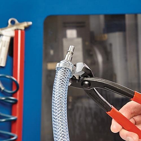 Gros plan d'une main utilisant une pince pour fixer un raccord de tuyau à un tuyau transparent. L'arrière-plan est flou.