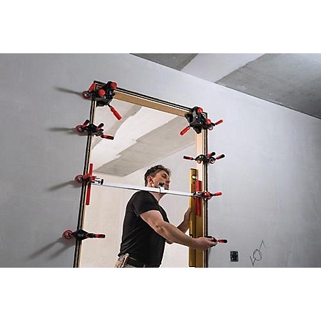 Un homme fixe un cadre de porte avec des pinces. Il utilise un niveau à bulle pour vérifier l'alignement.