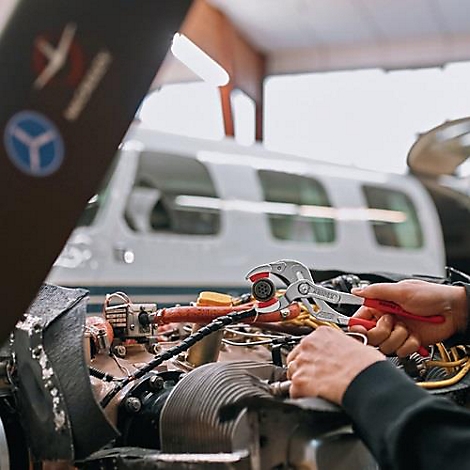 Un mécanicien répare un moteur d'avion avec une pince. En arrière-plan, un avion dans un atelier.