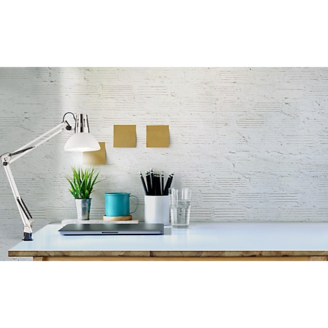 Desk with lamp, plant, pens, mug and laptop in front of a white brick wall.