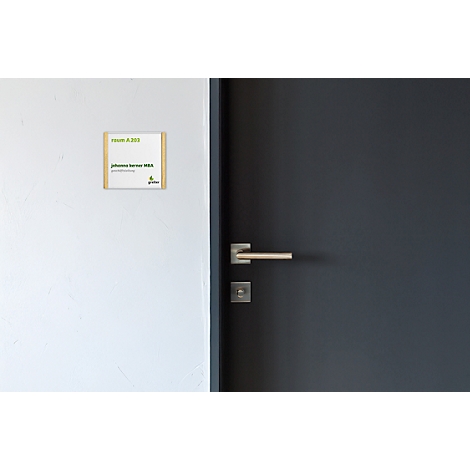 Un panneau avec le nom et le numéro de la chambre sur un mur blanc, à côté d'une porte noire avec une poignée argentée.