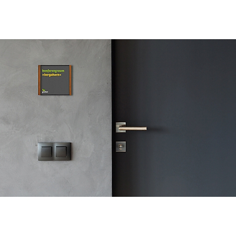 Mur gris avec porte, panneau de porte et interrupteurs. Le panneau indique : Salle de conférence Bergahorn.