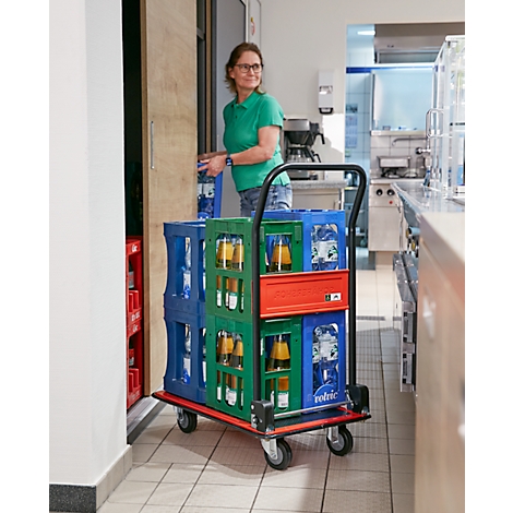 Vrouw met bril duwt een drankwagen met kratten door een gang.