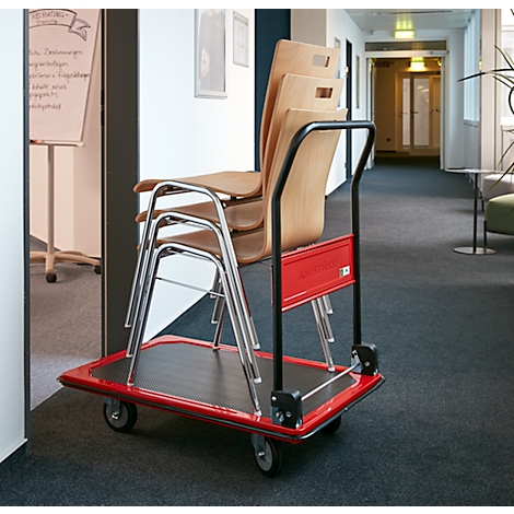 Een rode transportwagen met drie houten stoelen en twee opgevouwen metalen stoelen in een gang.