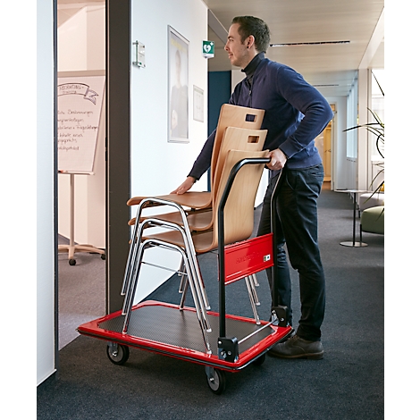 Man draagt stoelen met een rode transportwagen door een gang.