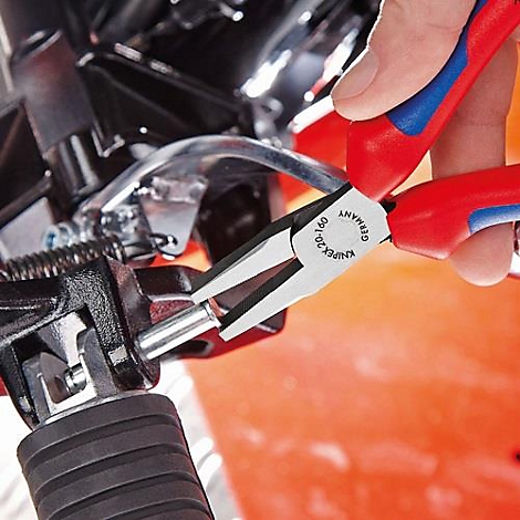 Close-up van een persoon die aan een motorfiets werkt met een rode en blauwe KNIPEX-tang. De tang grijpt een metalen pin.