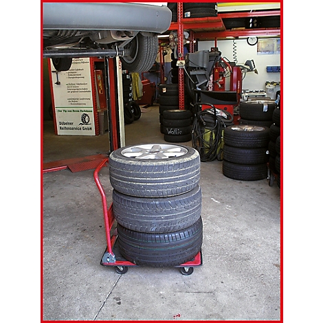 Vier Reifen auf einem roten Wagen in einer Werkstatt; ein Auto wird repariert.
